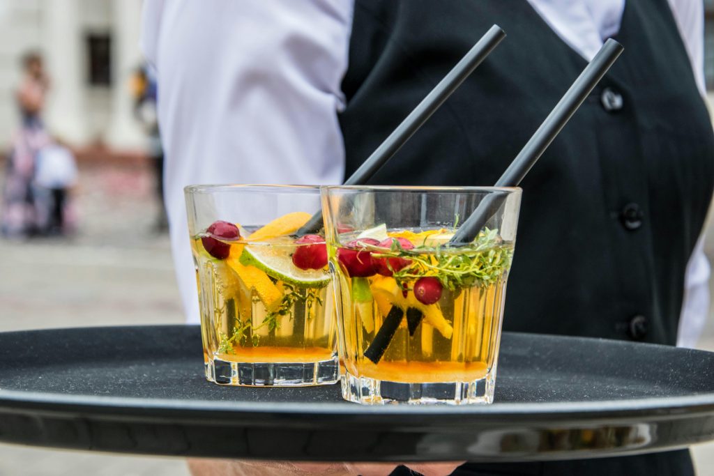 Catering Delicious orange cocktails with cranberries and herbs on a tray, served by waiter at an outdoor event.